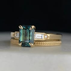 two gold rings with an emerald colored stone and diamond accented bands on top of each other