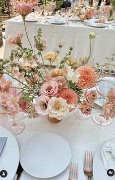 the table is set with white plates, silverware and pink flowers in vases