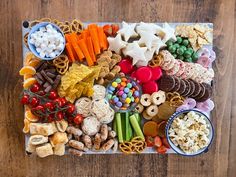 a platter filled with different types of snacks on a wooden table next to bowls of candy and pretzels