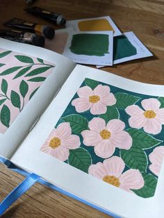 an open book with pink flowers and green leaves on the pages next to some markers