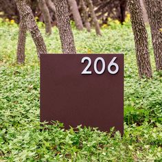 a brown sign sitting in the middle of a forest filled with green grass and trees