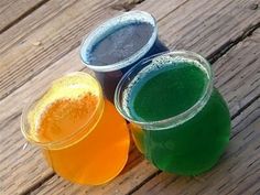 three different colored drinks sitting next to each other on a wooden table with wood planks