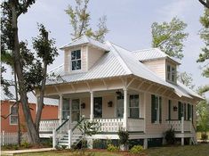 a small white house with porches on the front and side of it, surrounded by trees