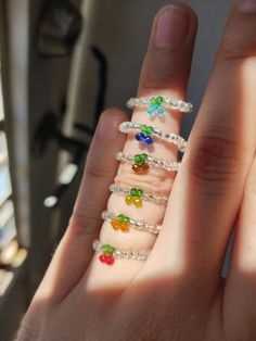 a person's hand with five different colored rings on their fingers and one is holding something in the other hand