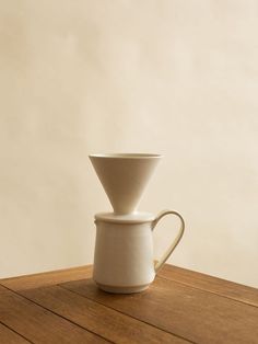 a white coffee pot sitting on top of a wooden table next to a cup filled with liquid