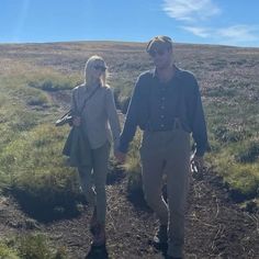 a man and woman walking down a dirt path in the middle of an open field