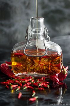 a glass bottle filled with liquid sitting on top of a table next to chili peppers