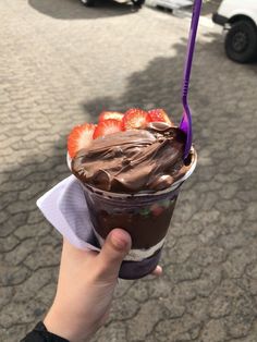 a person holding up a cup with chocolate and strawberries in it on the street