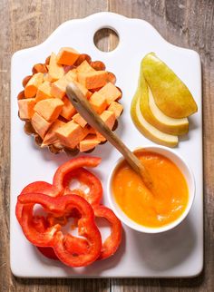 a white plate topped with cut up vegetables and sauces next to an apple on top of a cutting board