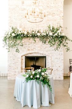 a table with white flowers and greenery is set up in front of a fireplace