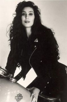 black and white photograph of a woman sitting on top of a motorcycle with her hand on the handlebars