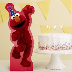 a birthday cake with candles in the shape of a sesame street character standing next to it