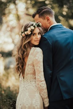 a man and woman standing next to each other in front of trees with flowers on their head