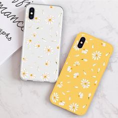 two iphone cases sitting next to each other on top of a white table with flowers