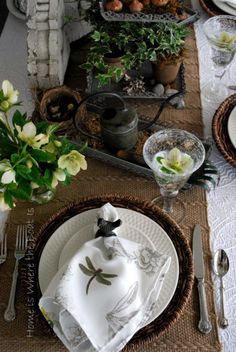 the table is set with dishes, silverware and flowers in vases on it