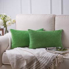 two green pillows sitting on top of a white couch next to a vase with flowers