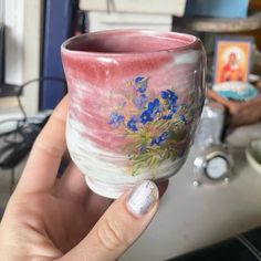 a hand holding a cup with flowers painted on it