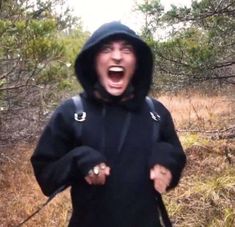 a man with his mouth open in the middle of a wooded area wearing a hoodie