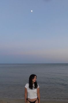 a woman standing on top of a beach next to the ocean under a blue sky