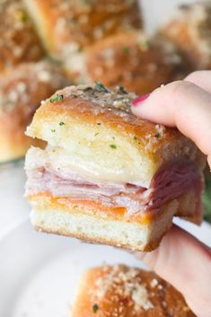 a hand holding a ham and cheese sandwich on a plate with other pastries in the background