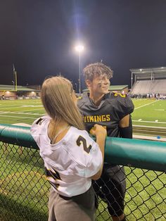 two people standing next to each other near a fence on a football field at night