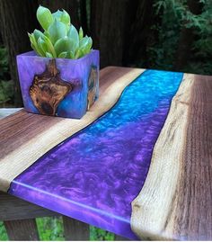 a wooden table topped with a purple vase filled with green plant sitting on top of it