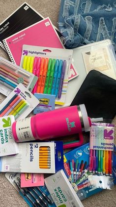 a pile of school supplies including pens, markers and pencils on the floor next to a book