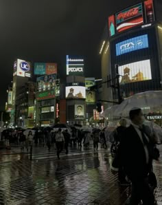 many people are walking on the street in the city at night with their umbrellas open