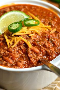 a white bowl filled with chili and cheese next to a slice of lime on the side