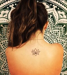 the back of a woman's neck with a lotus tattoo on her left shoulder