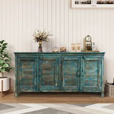 an old blue dresser with flowers and pictures on the top, next to a potted plant