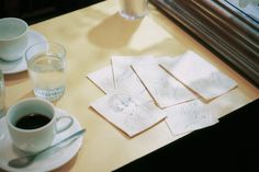 coffee cups and saucers on a table next to some papers with drawings in them