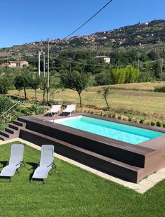 an empty swimming pool in the middle of a grassy area with lounge chairs around it