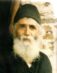 an old man with a long white beard wearing a black beanie and standing in front of a brick wall