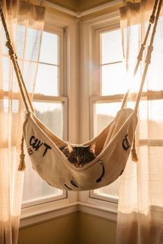 a cat is laying in a hammock hanging from a window sill with curtains