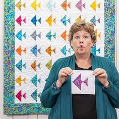 a woman holding up a piece of paper in front of a quilt