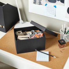 an office desk with pens, pencils and other items in a box on it