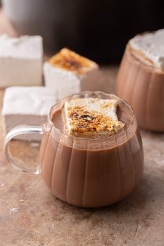 two mugs filled with hot chocolate and marshmallows on top of a table