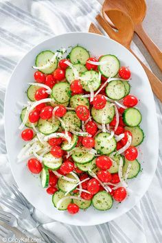 cucumber and tomato salad in a white bowl with wooden spoon on the side