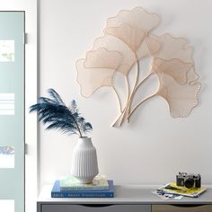 a white vase sitting on top of a table next to a wall mounted flower sculpture