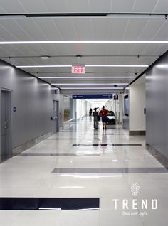 two people are walking down the hallway in an office building with exit signs above them