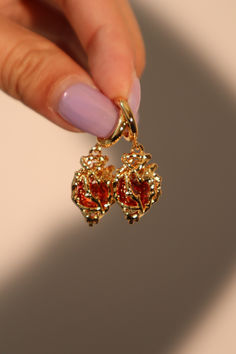 Our 18K Red Heart Earrings are ethereal. This pair of earrings is adorned with high quality zirconia red gems that sparkle and shine angelically. When you can’t decide on a look, match these earrings with your outfit to be your saving grace! Red Crystal Earrings, Red And Gold Accessories, Gold Jewelry Earrings Simple, Cool Gold Earrings, Earring Outfit Ideas, Red And Gold Earrings, Gold And Red Jewelry, Prom Jewelry Gold, Red And Gold Aesthetic