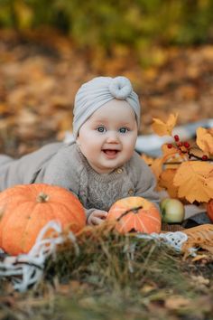 a baby laying on the ground next to pumpkins and other autumn leaves, smiling at the camera