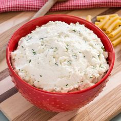 a red bowl filled with mashed potatoes on top of a cutting board next to fries