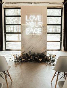 two white chairs sitting in front of a wall with love your face written on it