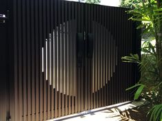 a large black gate in the middle of some plants and trees with an interesting design on it