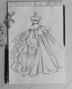 a drawing of a dress on paper next to a pen and flower vase with flowers in it