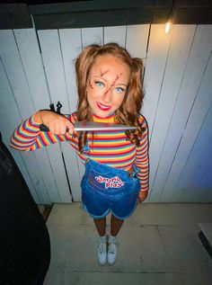 a woman with makeup on her face is standing in front of a wall holding a knife