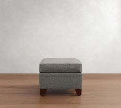 a gray ottoman sitting on top of a hard wood floor next to a white wall