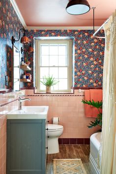 a bathroom with pink and blue wallpaper has a toilet, sink, tub, and shower curtain